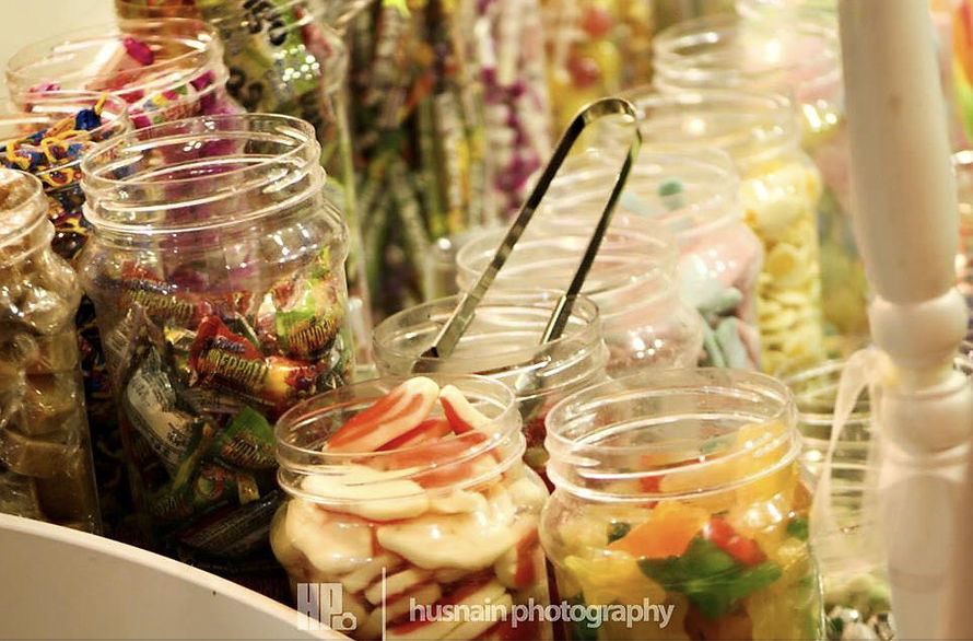 Two rows of jars containg various sweets, one with tongs in it.